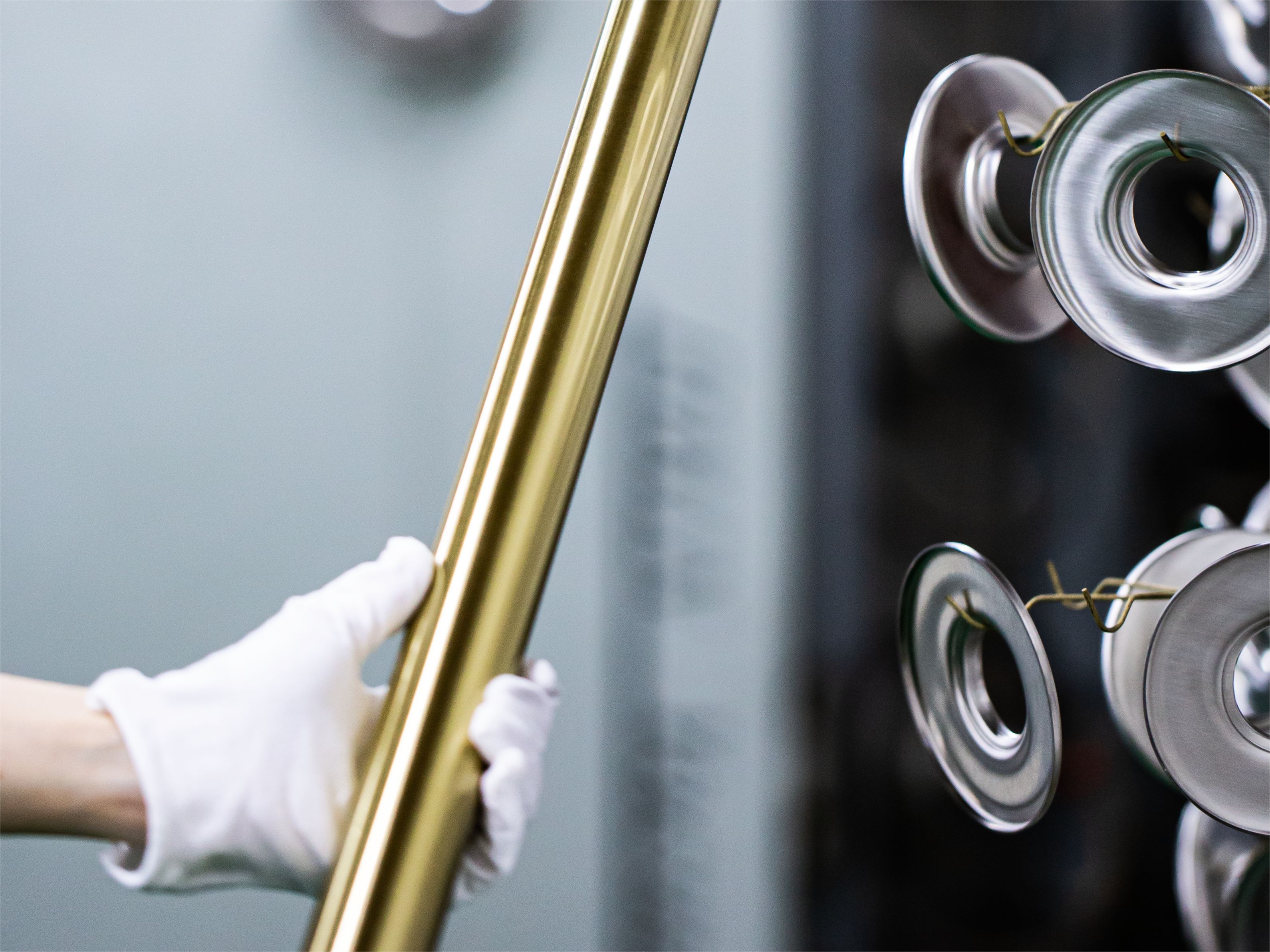 Technician from Foshan AussieSteel Metal Products Co., Ltd. inspecting a champagne-gold stainless steel tube with white gloves. The background shows polished steel parts, highlighting AussieSteel’s precision surface finishing and quality control expertise.